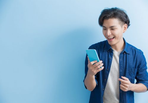 man student smile and use phone isolated on blue background,asian