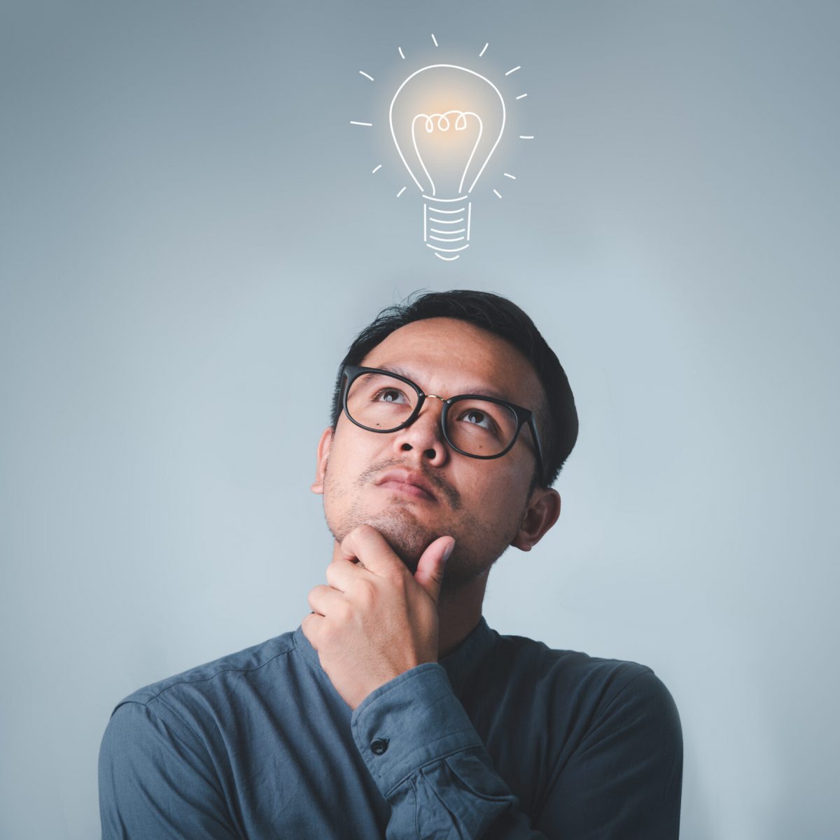 Thinking asian man in glasses looking up with light idea bulb above head on gray background.creative idea.Concept of idea and innovation